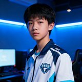 一位16岁左右的短发少年，眼神专注，穿着电竞牛青训营统一队服，身后是训练室的蓝色灯光
